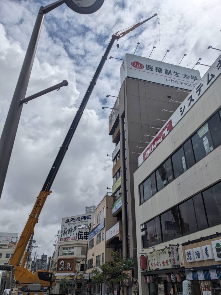 いわき駅前のビル上部へ大型看板をクレーンで取り付ける作業